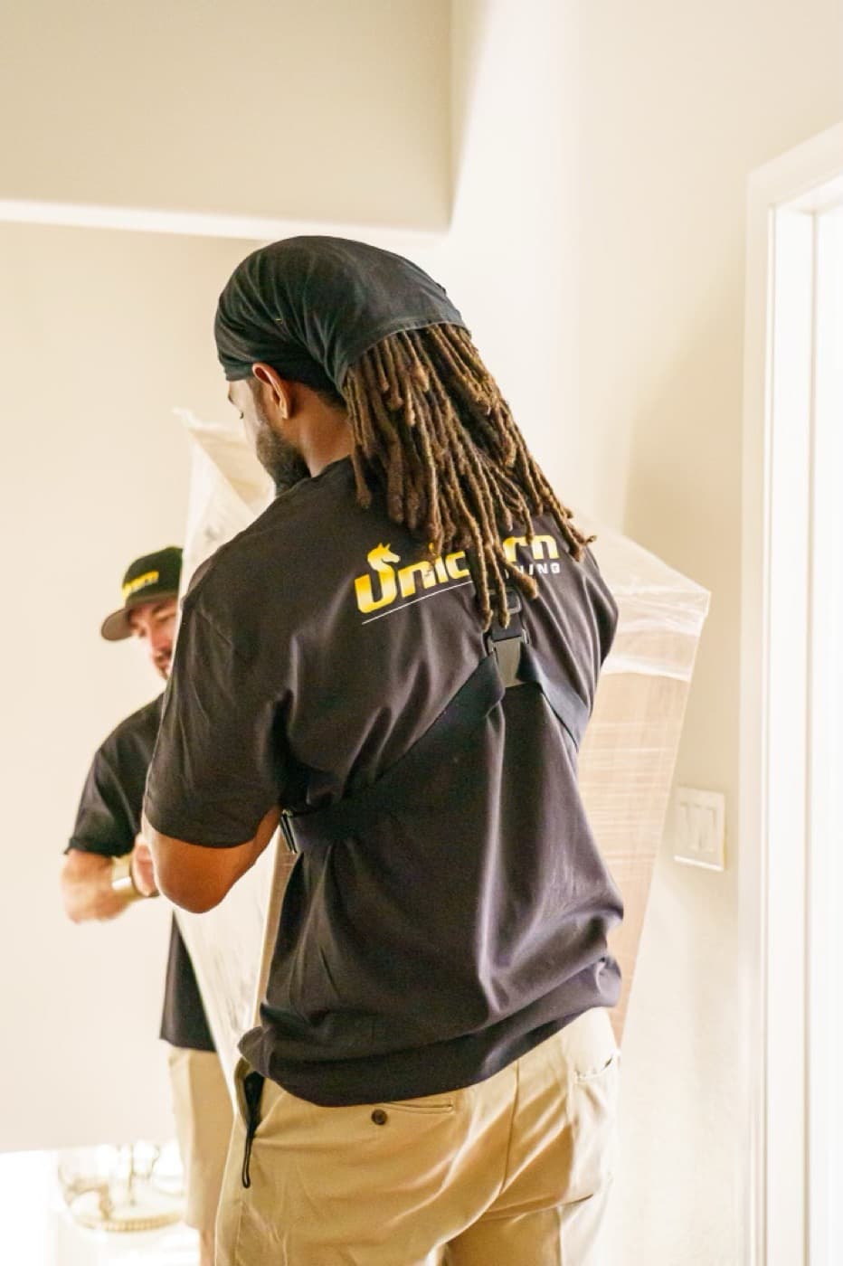 Two Unicorn Moving crew members carrying a wrapped item together through a home